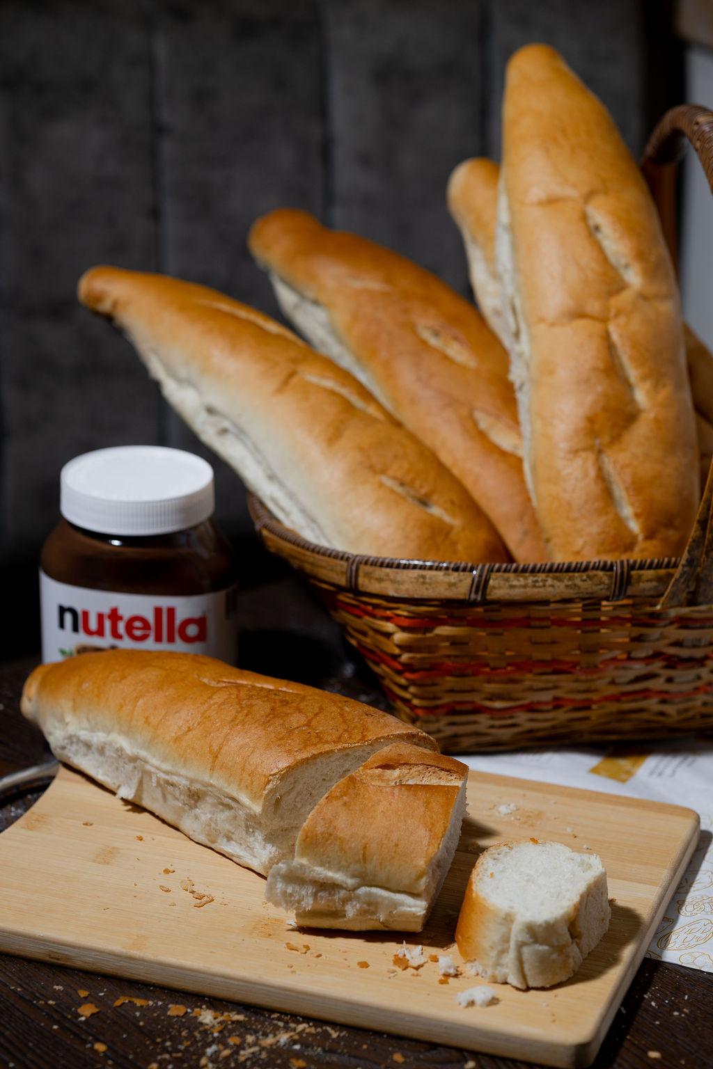 A basket of golden Jessy Bread baguettes with a fresh loaf sliced on the board